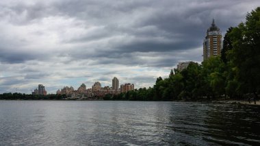 sakin nehir manzarası ve bulutlu gökyüzü arka planındaki ağaçların arkasındaki binalar, doğa kavramı, Kyiv, Ukrayna