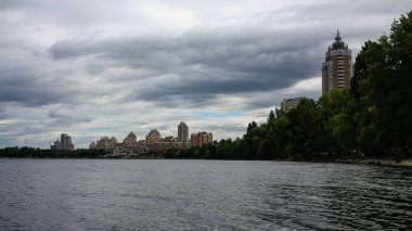 sakin nehir manzarası ve bulutlu gökyüzü arka planındaki ağaçların arkasındaki binalar, doğa kavramı, Kyiv, Ukrayna