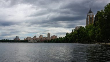 sakin nehir manzarası ve bulutlu gökyüzü arka planındaki ağaçların arkasındaki binalar, doğa kavramı, Kyiv, Ukrayna