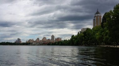 sakin nehir manzarası ve bulutlu gökyüzü arka planındaki ağaçların arkasındaki binalar, doğa kavramı, Kyiv, Ukrayna