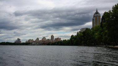 sakin nehir manzarası ve bulutlu gökyüzü arka planındaki ağaçların arkasındaki binalar, doğa kavramı, Kyiv, Ukrayna