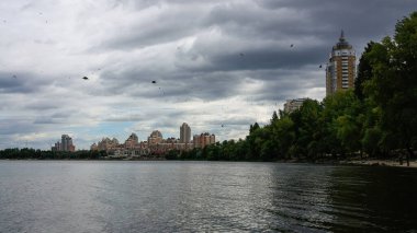 sakin nehir manzarası ve bulutlu gökyüzü arka planındaki ağaçların arkasındaki binalar, doğa kavramı, Kyiv, Ukrayna