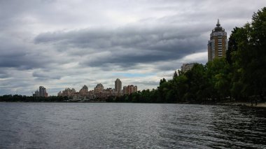 sakin nehir manzarası ve bulutlu gökyüzü arka planındaki ağaçların arkasındaki binalar, doğa kavramı, Kyiv, Ukrayna