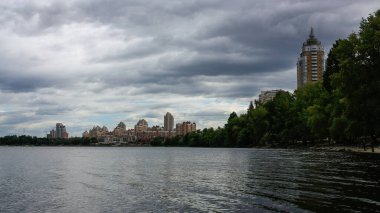 sakin nehir manzarası ve bulutlu gökyüzü arka planındaki ağaçların arkasındaki binalar, doğa kavramı, Kyiv, Ukrayna