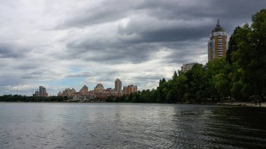 sakin nehir manzarası ve bulutlu gökyüzü arka planındaki ağaçların arkasındaki binalar, doğa kavramı, Kyiv, Ukrayna