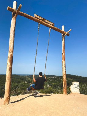 man riding a giant swing on a mountain overlooking the mountain nature vertical