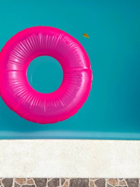 round pink float floating in a pool of blue water and a small leaf of tree