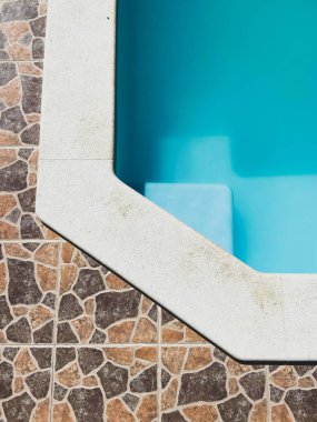 corner of the pool with ladder, blue water and tiles on the vertical floor