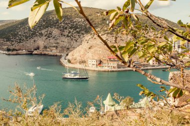 Ufukta, Balaklava Körfezi 'ne giriş yapan, zevkli bir yelkenliyle güzel bir deniz manzarası. Dağ manzarası, ağaçlar. Sonbaharın başında. Günaydın..