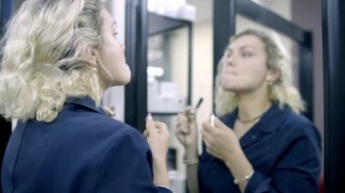 Sarışın ve ayna yansıması, dudakları boyuyor.