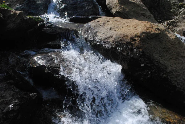 Kayalık bir nehirdeki şelalede su bir taştan diğerine akar.