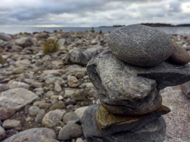 : Taşlardan yapılmış bir meditasyon figürü, bulutlu bir günde Ladoga adalarına bakan kayalık bir plajın ortasında büyük bir taşın üzerine katlanmış.