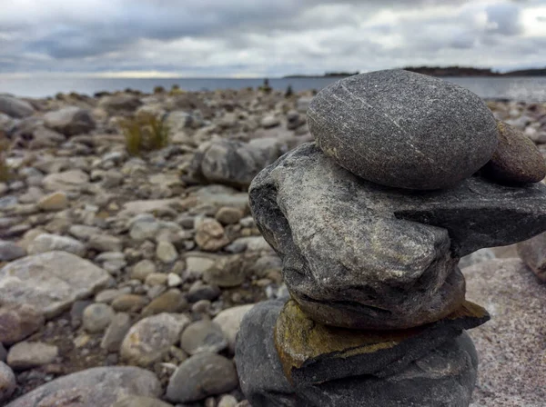 : A meditation figure made of stones, folded on a large stone in the middle of a rocky beach overlooking the Ladoga islands on a cloudy day