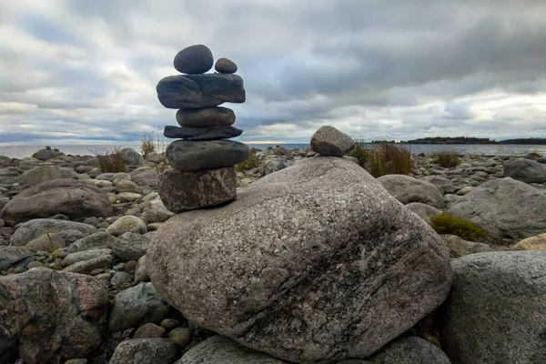 A meditation figure made of stones, folded on a large stone in the middle of a rocky beach overlooking the Ladoga islands on a cloudy day
