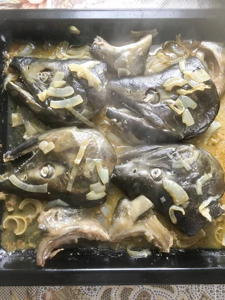 Lezzetli ev yapımı öğle yemeği. Tavada soğan pişmiş büyük balık kafaları.