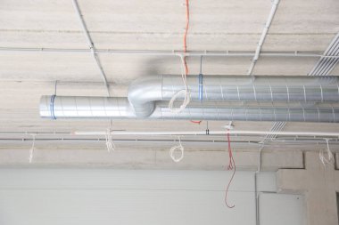 Beton yapısı olan sanayi binası, havalandırma boruları ve asma kabloları olan tavan.