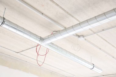 Beton yapısı olan sanayi binası, havalandırma boruları ve asma kabloları olan tavan.