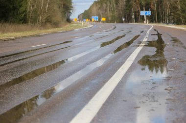 Su birikintileri, sarı işaretler, trafik işaretleri ve araçlar ile eski asfalt yol, onarım için hazırlanıyor