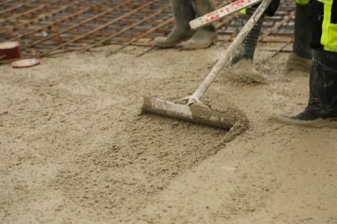 Construction worker leveling freshly poured concrete in a building foundation