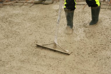 Construction worker leveling freshly poured concrete in a building foundation