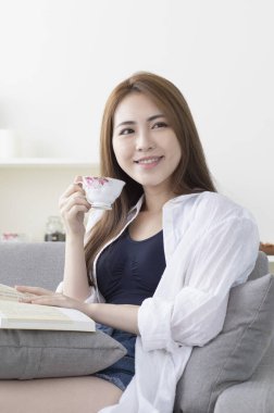 Kanepede oturup kitap okuyan genç bir kadın.