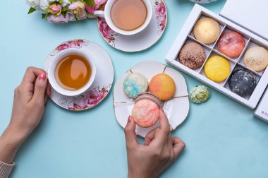 woman holding delicious macaron. Cups of tea with macaroons on blue background