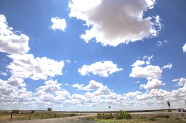 Bir tarlası ve mavi gökyüzünde beyaz bulutları olan güzel bir manzara. 