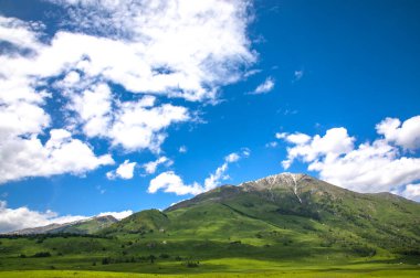 Güneşli bir havada, yeşil dağları ve mavi gökyüzünü olan güzel bir manzara.