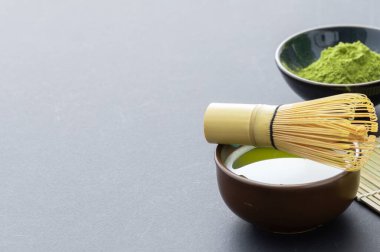 Bir fincan sıcak kibrit çayı, kasede kibrit tozu ve beyaz arka planda bambu çırpısı.