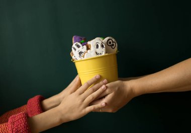 Annenin elleri, çocuğun ellerine hayalet ve balkabağı şeklinde zencefilli ekmek dolu bir kova verir. Cadılar Bayramı kutlaması için hazırlık kavramı. Boşluğu kopyala