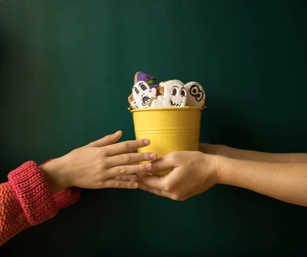 Mother`s hands pass a bucket filled with gingerbreads in the form of ghosts and pumpkins into the child\'s hands.  Concept of preparation for the celebration of Halloween. Copy space