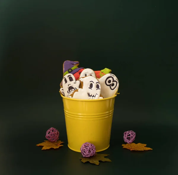 A yellow bucket filled with gingerbreads in the form of ghosts and pumpkins as sweet presents for children on Halloween party.  Concept of preparation for the celebration of Halloween. Copy space