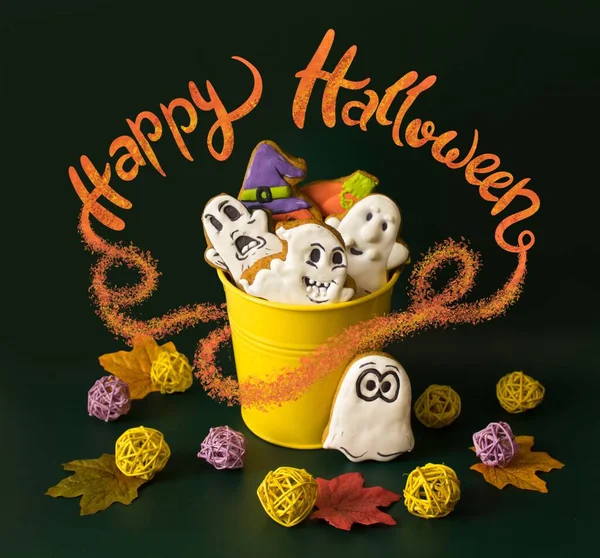 A yellow bucket filled with gingerbreads in the form of ghosts and pumpkins as sweet presents for children on Halloween party.  Concept of preparation for the celebration of Halloween.