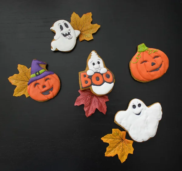 Colorful freshly baked and colored gingerbread in the form of ghosts and pumpkins as sweet gifts for children on Halloween. Black backgound. The concept of preparing for the celebration of Halloween.