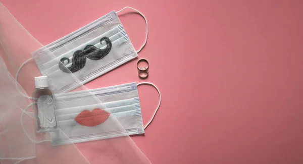 Pembe arka planda iki alyans ve bıyıklı koruyucu yüz maskeleri var. Coronavirus COVID-19 salgını sırasında düğün töreni konsepti. Pankart