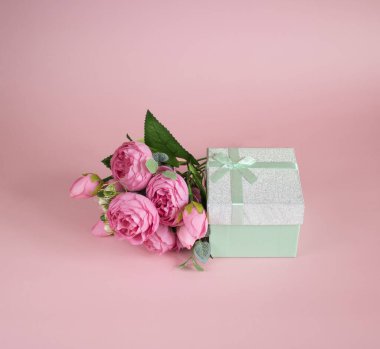 Hediye kutusu ve pembe arka planda bir buket çiçek. Sevgililer Günü, doğum günü, Uluslararası Kadınlar Günü ve diğer tatiller için tebrik konsepti.