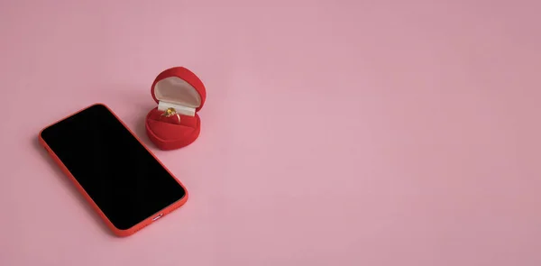 New smartphone and engagement ring in red gift box next to orchid branch on pink background. The concept of best gift for Valentine\'s Day, birthday, International Women\'s day and other holidays.