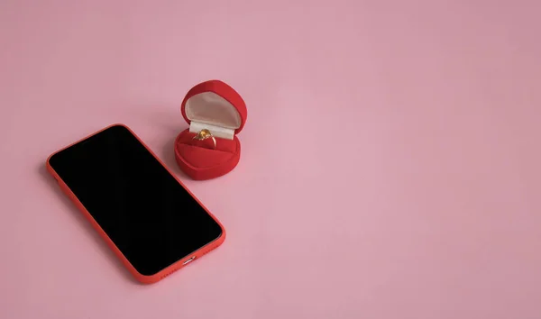 New smartphone and engagement ring in red gift box next to orchid branch on pink background. The concept of best gift for Valentine\'s Day, birthday, International Women\'s day and other holidays.