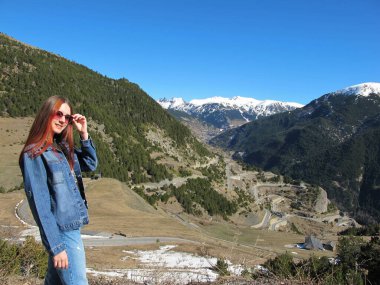 Kızıl saçlı bir kız parlak mavi gökyüzüne karşı dağın manzarasına bakıyor. Seyahat içeriği