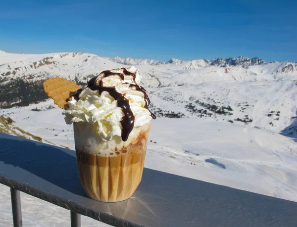 Krem şantili ve çikolata soslu taze yapılmış kahve içeceği karla kaplı dağların arka planına ve parlak mavi gökyüzüne karşı. Seyahat içeriği