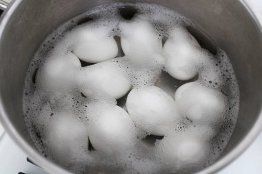 Beyaz yumurtaları siyah zemin üzerinde kaynayan suyun içinde paslanmaz bir tencerede kaynatma işlemi. Paskalya Bayramından önce yumurta boyama hazırlığı.