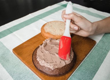 Genç bayan evde küçük bir pasta hazırlıyor. İki sünger keki ve aralarında krema katmanı, rendelenmiş acı çikolatalı çikolata ganacından oluşuyor. Evde kek pişirme süreci. Adım adım tarifli fotoğraf serileri