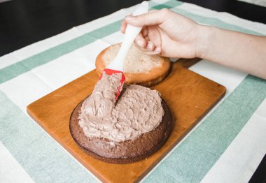 Genç bayan evde küçük bir pasta hazırlıyor. İki sünger keki ve aralarında krema katmanı, rendelenmiş acı çikolatalı çikolata ganacından oluşuyor. Evde kek pişirme süreci. Adım adım tarifli fotoğraf serileri