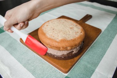 Genç bayan evde küçük bir pasta hazırlıyor. İki sünger keki ve aralarında krema katmanı, rendelenmiş acı çikolatalı çikolata ganacından oluşuyor. Evde kek pişirme süreci. Adım adım tarifli fotoğraf serileri