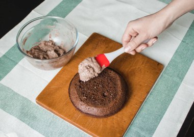 Genç bayan evde küçük bir pasta hazırlıyor. İki sünger keki ve aralarında krema katmanı, rendelenmiş acı çikolatalı çikolata ganacından oluşuyor. Evde kek pişirme süreci. Adım adım tarifli fotoğraf serileri