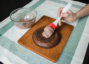 Genç bayan evde küçük bir pasta hazırlıyor. İki sünger keki ve aralarında krema katmanı, rendelenmiş acı çikolatalı çikolata ganacından oluşuyor. Evde kek pişirme süreci. Adım adım tarifli fotoğraf serileri