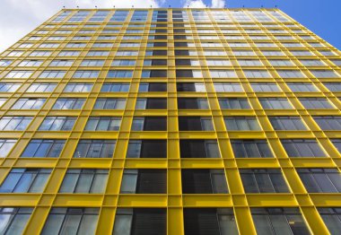 Güzel sarı bina ve bulutlu gökyüzü. Modern apartman dairesi konsepti. Açık hava yerleşim tesisi. Modern mimarinin düşük açılı görüntüsü