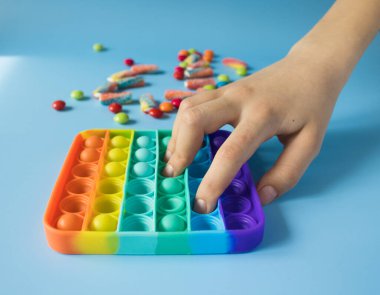 Çocuk gökkuşağı Pop ile oynuyor renkli cereyan ve kalp şeklinde marmelatların yanında oyuncak kıpırdıyor. Patlat - mavi arka plandaki çocuklar için yeni bir stres önleyici oyuncak.
