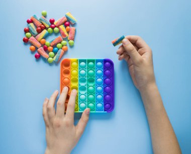 Çocuk gökkuşağı Pop ile oynuyor renkli cereyan ve kalp şeklinde marmelatların yanında oyuncak kıpırdıyor. Patlat - mavi arka plandaki çocuklar için yeni bir stres önleyici oyuncak.