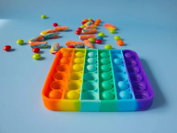 Gökkuşağı şekeri renkli içki ve marmelatların yanında hareketli oyuncak. Patlat - mavi arka plandaki çocuklar için yeni bir stres önleyici oyuncak.